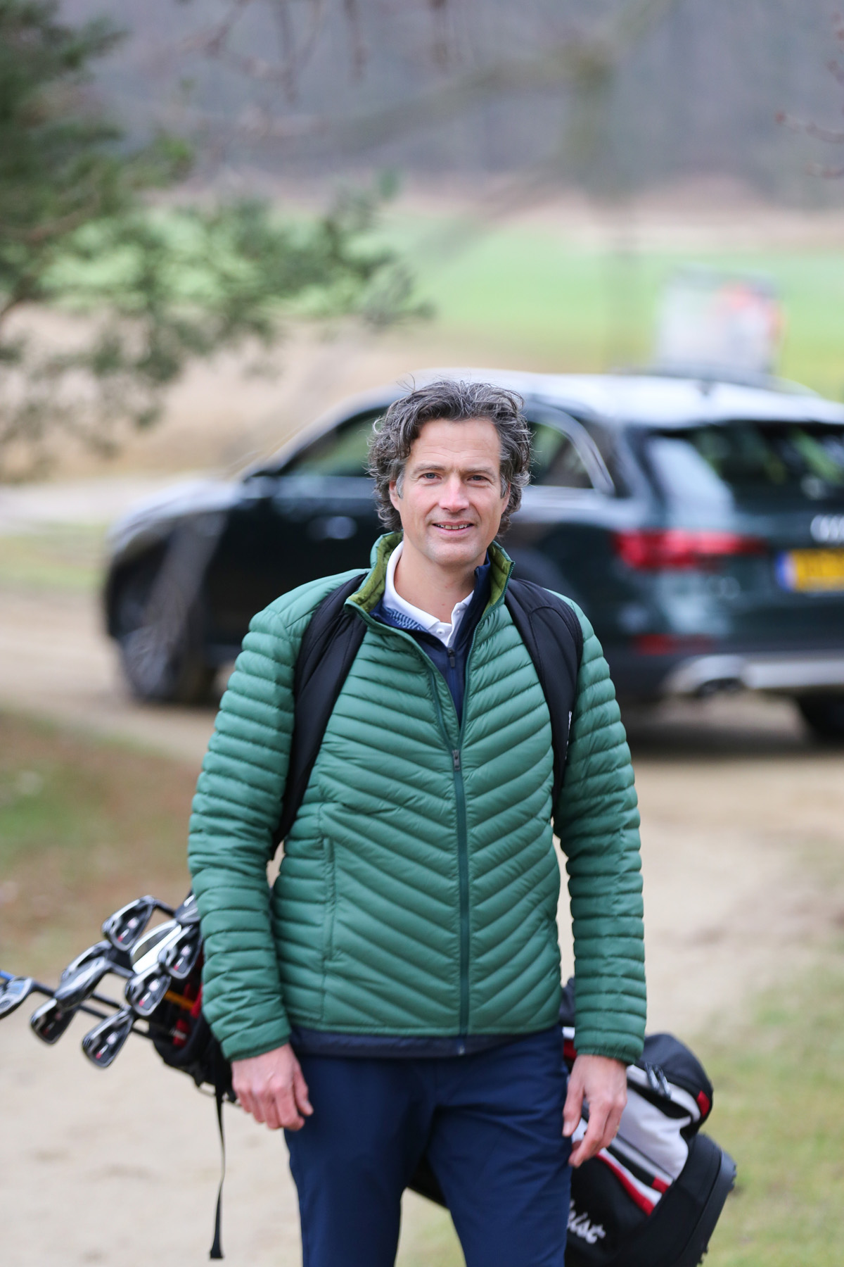Zakelijk portret van een man met golfspullen bij een bedrijfsauto