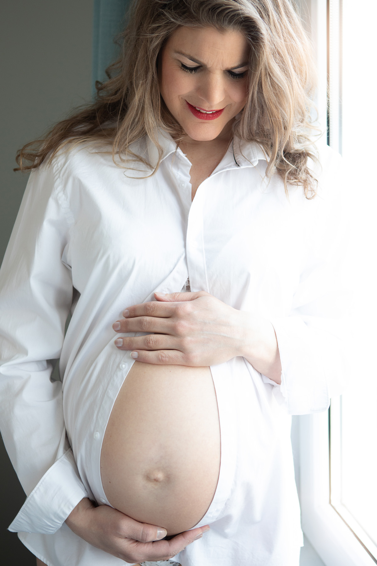 Zwangere vrouw in witte blouse bij het raam